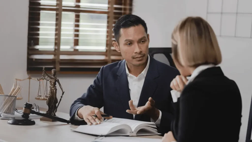 Attorney consulting with client about legal strategy at office desk with scales of justice