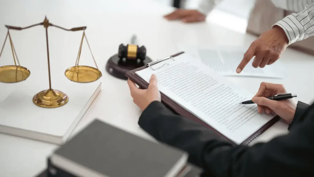 Two attorneys reviewing legal documents at a desk with a gavel and scales of justice, discussing how much attorneys should invest in promotion strategies