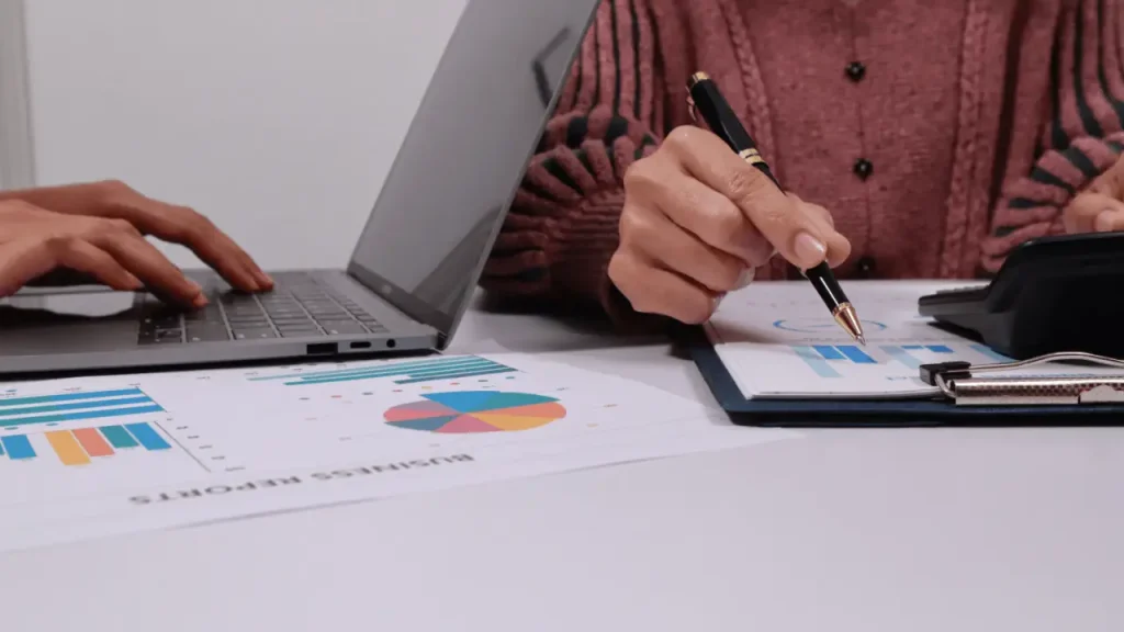 Attorney analyzing client acquisition data on laptop with business reports and charts on desk