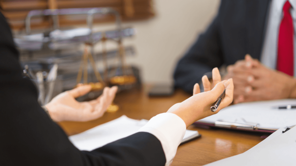 Two attorneys discussing legal strategy at a law office desk with scales of justice in the background