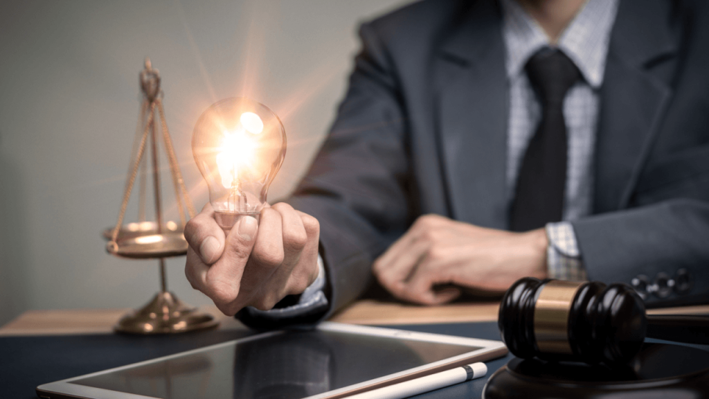 Attorney holding a glowing light bulb beside scales of justice and a gavel